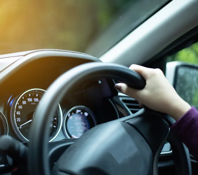 Close-up of a driver’s hand on the steering wheel beside the vehicle’s instrument panel