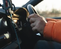 Close-up of a driver’s hands on the steering wheel beside a mounted smartphone