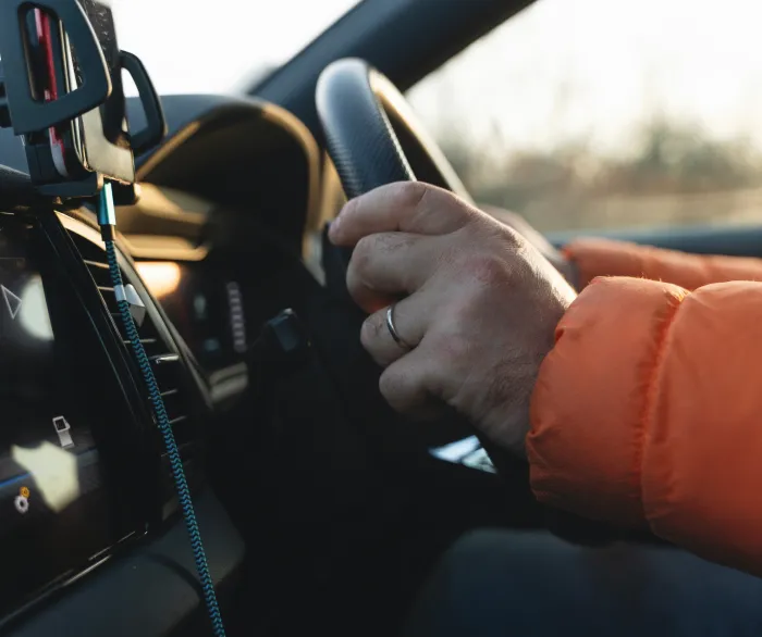 Close-up of a driver’s hands on the steering wheel beside a mounted smartphone