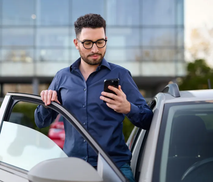 Employee checking a smartphone while standing beside a car